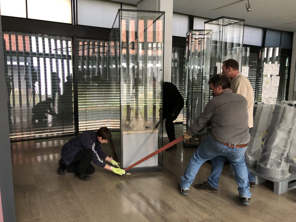 Vier Mitarbeiter ziehen mit einem Seil eine Vitrine herum.