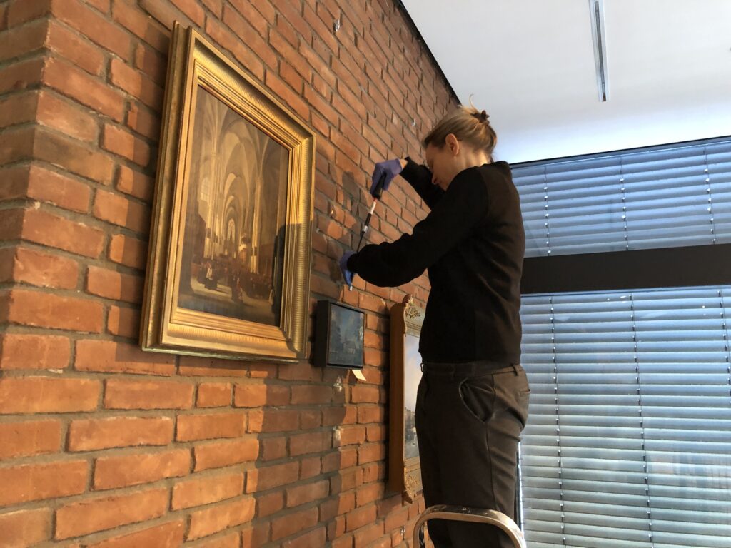 Eine Restauratorin schraubt Bilder von der Wand.